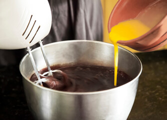 Pastry chef pouring ingredients into mixing bowl with mixer