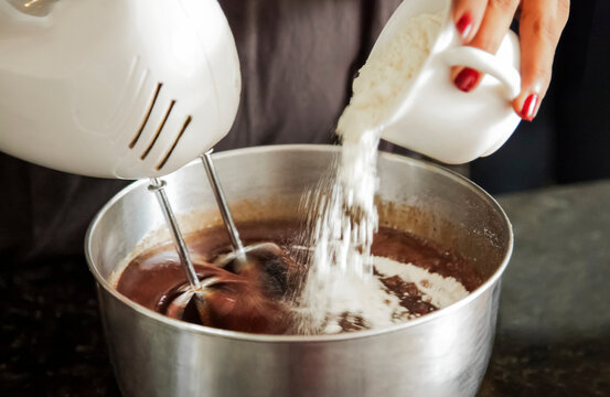 Close up of chef pouring flour into chocolate cake batter with mixer running