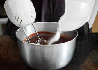 Pastry chef adding sugar to chocolate cream with mixer