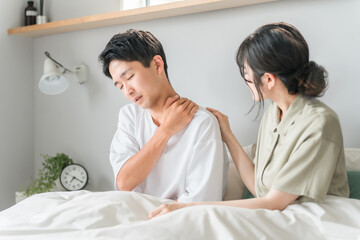 Obraz premium 朝寝室で肩こりに悩む男性と心配する女性・夫婦・カップル 