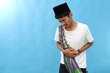 Asian muslim man squeeze his stomach for having stomachache pain, against blue background