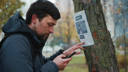 A man reads an advertisement about the loss of a dog in a tree in the park and calls the owner at the phone number indicated in the poster. The theme of the missing search for missing pets. Lost dog