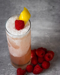 Raspberry cocktail set on top of a stone surface surrounded by raspberries
