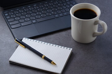 コーヒーを飲みながら、キーボードを接続したタブレット端末とメモ帳、ペンで、デスクワーク中のイメージ
