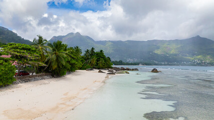 Beach with bright blue water and dense greenery under a cloudy sky. Seychelles, Mahe. Beau Vallon...