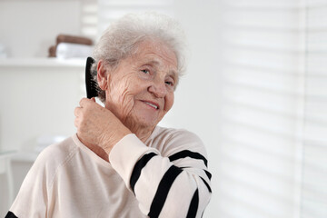 Senior woman brushing her hair with comb at home, space for text