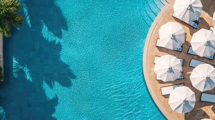 Aerial view of sunlit pool with white umbrellas and loungers near blue water