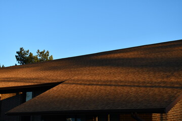 Long shadows cast over large brown shingled roof.