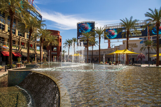 the Westgate Entertainment District with restaurants, retail stores,  a water fountain and lush green trees in Glendale Arizona USA