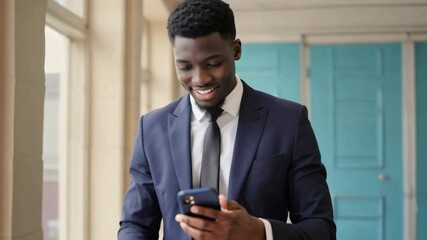 Smiling professional man in suit checks his phone in bright office setting.