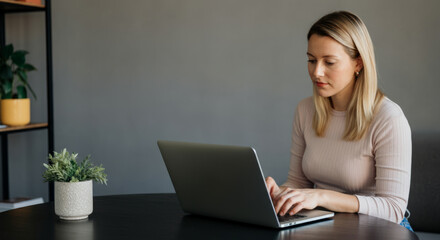 Fototapeta premium Female caucasian adult typing on laptop in modern home office with plant decor