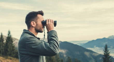 Young caucasian male observing mountain scenery with binoculars