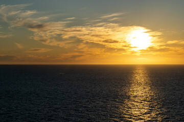 The sun sets on the horizon over the ocean, with colorful and cloudy skies along the coast of Baja California, Mexico.