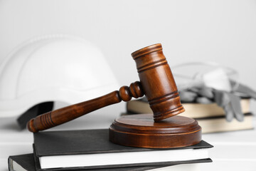 Accident at work concept. Gavel, books and construction worker's protective gear on white wooden...