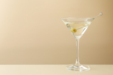 Martini cocktail with olive in glass on beige table, space for text