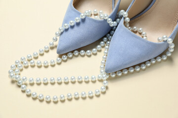 Stylish shoes and pearl necklace on beige background, closeup