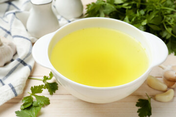 Tasty chicken bouillon in bowl and ingredients on wooden table, closeup