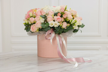 Gift box with bouquet of beautiful flowers and eucalyptus branches on marble table against white wall
