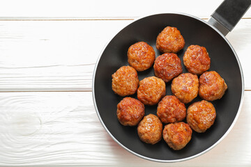 Tasty meatballs in frying pan on white wooden table, top view. Space for text