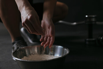 Woman applying talcum powder onto her hands above bowl before training in gym, closeup