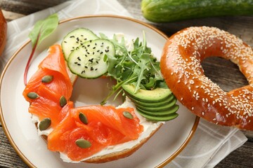 Delicious bagel with salmon, cream cheese, cucumber, avocado and pumpkin seeds on table, closeup