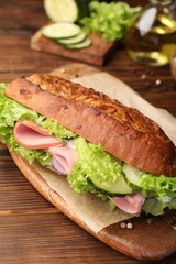 Delicious baguette sandwich with ham on wooden table, closeup