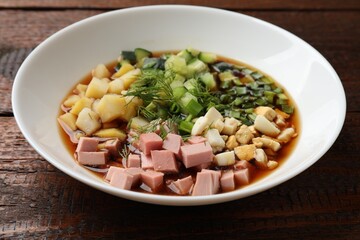 Tasty okroshka soup with kvass in bowl on wooden table, closeup