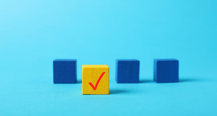 One yellow cube with check mark among others on light blue background, selective focus