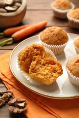 Tasty carrot muffins, fresh vegetables and walnuts on wooden table, closeup