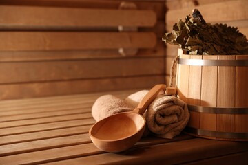 Bucket, whisk, ladle and towels on wooden bench in sauna. Space for text