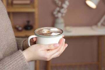Woman holding mug of tasty hot chocolate with marshmallows and cinnamon indoors, closeup. Space for text