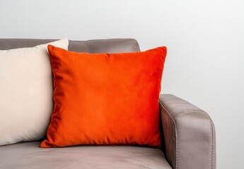 Close up view of an orange velvet pillow and an off white pillow resting on a gray couch against a white wall. Soft lighting, simple home decor