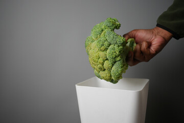 Broccoli being discarded into a white waste bin