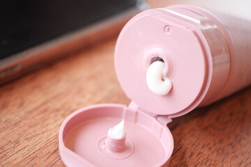 Squeezing moisturizing cream from a pink tube on wooden surface