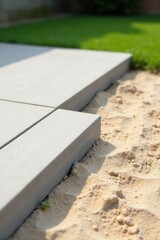 Grey paving stones being laid in a garden next to sandy soil during a sunny day