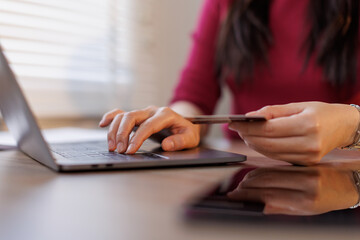 Asian female hand holding credit card while online paying using a laptop and card for online shopping, sitting at a wooden table 
