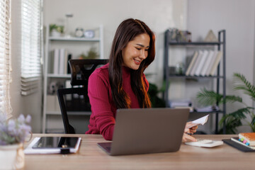 Obraz premium Calculator, budget and asian woman in home office with laptop, financial management and checking bills. Remote work, bookkeeping and freelancer with tax invoice, planning and online project cost.
