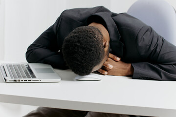 Exhausted businessman in suit resting head on desk beside laptop, overwhelmed with work and stress