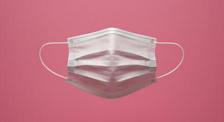 A close-up image of a disposable surgical face mask with elastic ear loops, set against a vibrant pink background with subtle light effects.