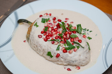 un chile relleno cubierto de nogada cremosa decorado con granada y perejil