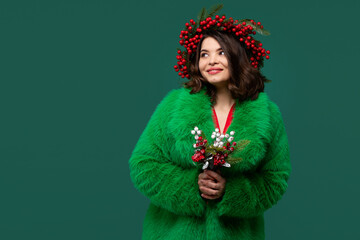 Woman in coat and red berry wreath gazes upward thoughtfully.