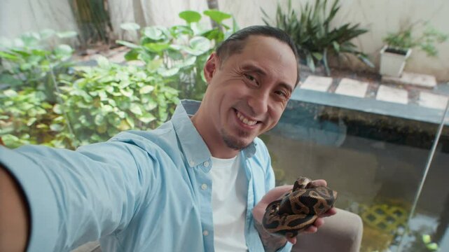 Medium close up POV of cheerful male owner taking selfie with small python snake