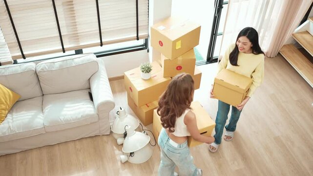 Couple of woman carrying box and arriving at new house at moving day. Top view of beautiful girl and friend walking and holding cardboard box while talking together and moving in the house. Myrmidon.