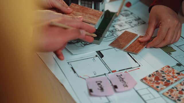 A vibrant scene capturing hands in collaboration over an interior design project. Colorful materials and floor plans are laid out, showcasing creativity and teamwork. SACTR