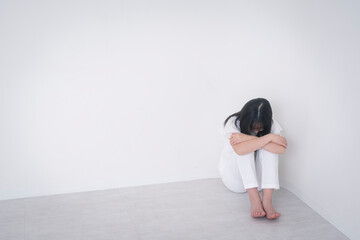 膝を抱えて座り、悩む女の子。スタジオ撮影白背景。