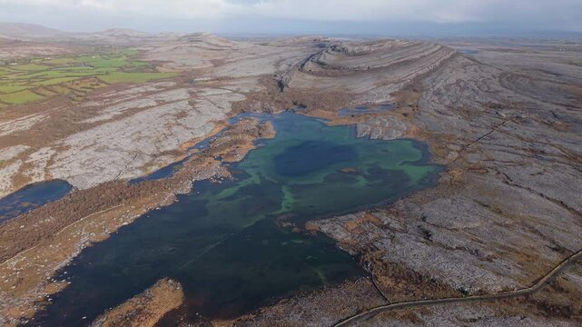 The Burren, County Clare, Ireland - A Scenic View of Rugged Limestone Terrain, Dark Lake Waters, and Distant Farmland - Aerial Drone Shot