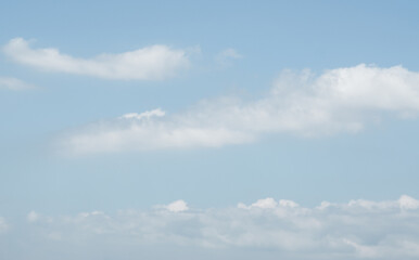  This image presents a clear blue sky with soft, fluffy white clouds floating peacefully