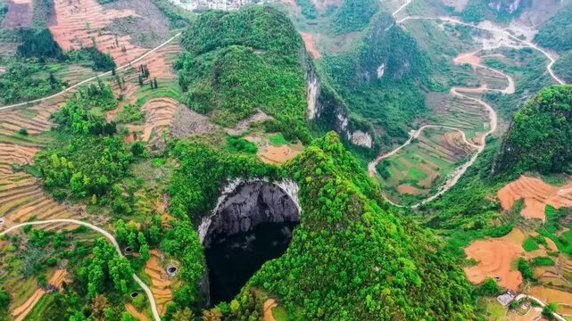 Aerial drone footage spinning around and over Xiaozhai Tiankeng or Heavenly Pit in Chine during a sunny day. Worlds deepest sinkhole in a mountain with trees and nature covering it. A road visible too