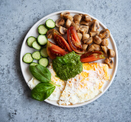 A full protein breakfast with vegetables and mushrooms on a plate. Fried eggs, champignons, tomatoes and green sauce.
