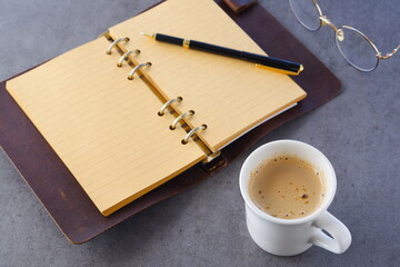 ミルクをたっぷり入れたコーヒー、カフェ・ラッテを飲みながら、システム手帳でデスクワークをしているイメージの写真素材
